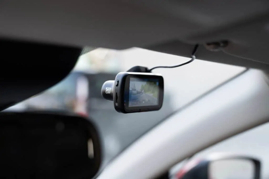 A product image for a dashboard camera to be used in cars; the image shows the dashcam mounted from the ceiling of the car facing forward out the windshield.